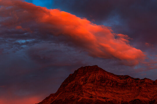 Dramatic glowing red cloud at sunset over a glowing mountain peak in Waterton Lakes National Park; Waterton, Alberta, Canada