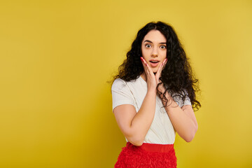 Young brunette woman with curly hair, wearing a red skirt, expresses emotions by covering her face with her hands.