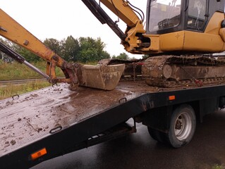 A small yellow excavator is loaded onto the tractor platform for transportation. Topics of construction and methods of moving construction equipment.