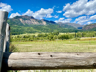 Behind a fence of a mountain view and a green pasture