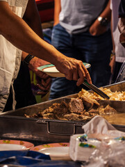 A person uses tongs to serve food from a large metal tray