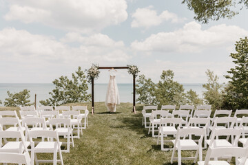 Outdoor lakeside wedding ceremony with a wedding dress hanging on arch