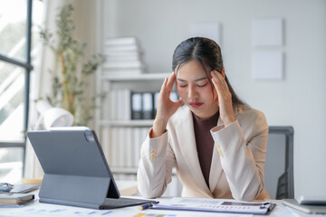 Stressed businesswoman in office with headache from work, feeling tired and overworked, showing importance of health in career
