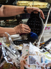 A person brushes a waffle iron with a blue brush, preparing it for use