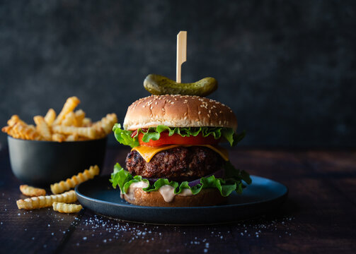 Hamburger and french fries on wood table with dark background.