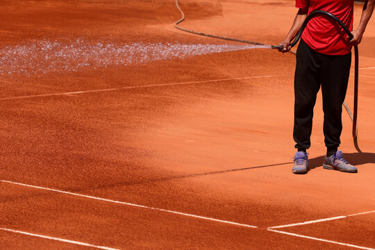 Maintenance personnel watering a clay tennis court.