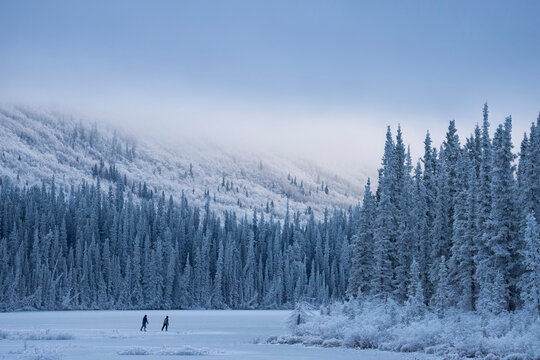 A couple of people skating on frozen Annie Lake surrounded by the beauty of a Yukon Winter; Whitehorse, Yukon, Canada