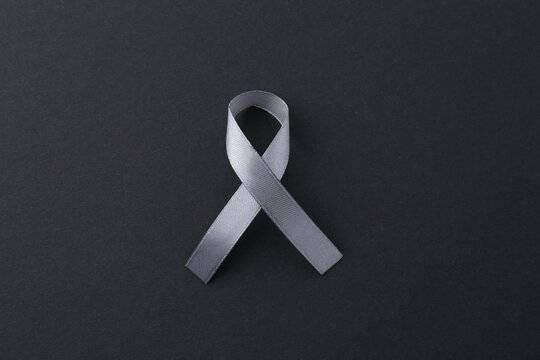 Grey awareness ribbon on black background, top view