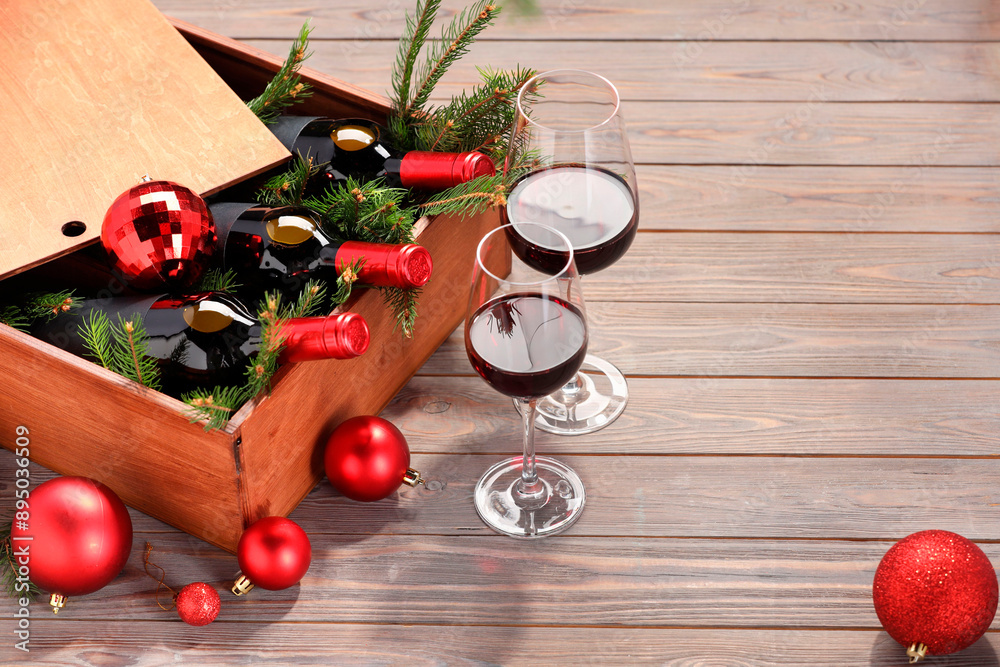 Sticker Wooden crate with bottles of wine, glasses, fir twigs and red Christmas balls on table. Space for text