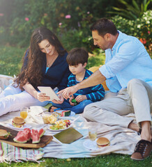 Naklejka premium Kid, picnic and parents on tablet at park, eating lunch and family bonding together in summer. Mother, child and dad on technology outdoor for learning, streaming and watch movie to relax with food