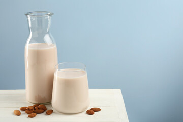 Fresh almond milk in carafe, glass and nuts on white wooden table, space for text