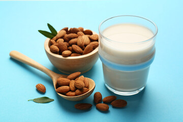Fresh almond milk in glass, nuts, spoon and green leaves on light blue background
