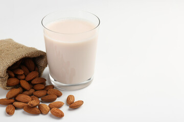 Fresh almond milk in glass, nuts and burlap sack on white background, space for text