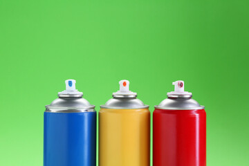 Many spray paint cans on green background, closeup. Space for text