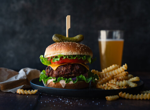 Hamburger, french fries and beer on wood table with dark background. - Powered by Adobe