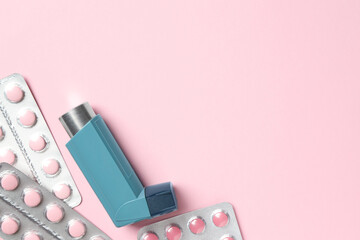 Asthma inhaler and pills on pink background, flat lay. Space for text