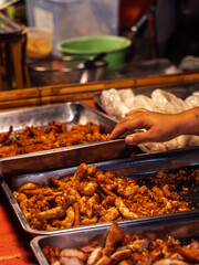 A hand reaches towards a tray of fried meat and garlic