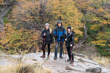 Three people are standing on a rocky hillside, wearing backpacks