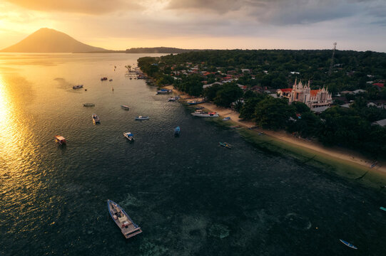 Boats moored off the coast of Bunaken at sunset, with a view of the church and Manado Tua in the background, North Sulawesi, Indonesia; Bunaken, North Sulawesi, Indonesia