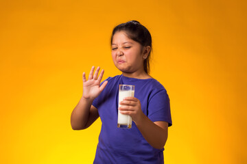 Kid girl with dairy allergy showing stop gesture front glass of milk on yellow background. Lactose intolerance concept