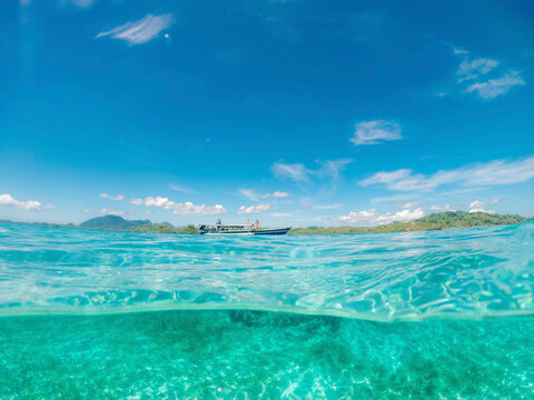 Split view of the clear turquoise ocean water and tourism dive boat along the coastline in Kepulauan Togean National Park; Wakai, Central Sulawesi, Indonesia