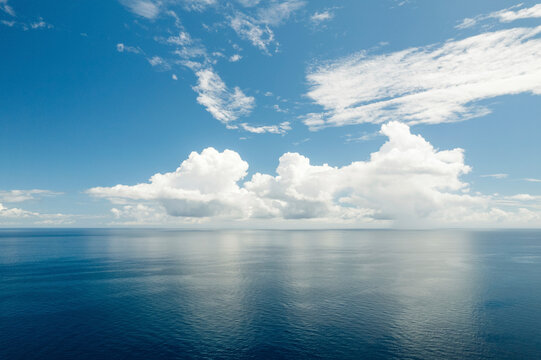 Bright clouds in a blue sky reflecting a mirror image into the tranquil blue water of the Molucca Sea at Kepulauan Togean National Park; Wakai, Central Sulawesi, Indonesia