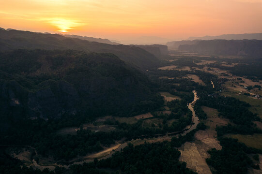 Silhouetted karst and farmland in a valley at sunset near Kong Lor Cave in Laos; Khammouane Province, Laos