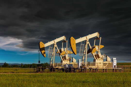 Two yellow pumpjacks in a green field with storm clouds in a dramatic dark sky, West of Airdrie; Alberta, Canada