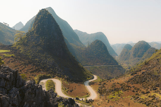 Road with switchback curves winding through a valley with peaked mountains in the countryside of Vietnam; Bao Tang Con Duong Hanh Phuc, Meo Vac District, Ha Giang, Vietnam