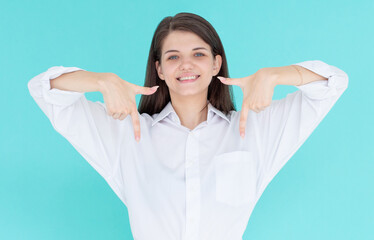 Smiling confident girl pointing fingers down to show advertisement, showing promo offer on bottom empty space, standing against blue background.