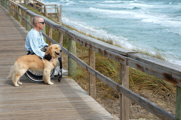 Paraplegic man in wheelchair with service dog enjoys the ocean view from a boardwalk; Boynton Beach, Florida, United States of America