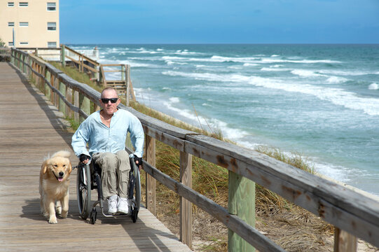 Paraplegic man in wheelchair with service dog enjoys the ocean view from a boardwalk; Boynton Beach, Florida, United States of America