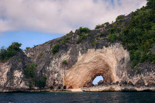 Natural arch along the beautiful coastline of Central Sulawesi, Indonesia, with lush vegetation on the rocky cliffs; Pasir Putih, Banggai Laut, Central Sulawesi, Indonesia