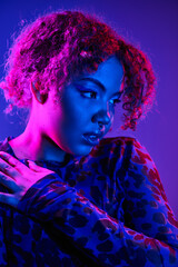 African American woman with curly hair poses in a vibrant leopard print shirt.