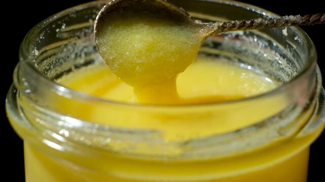 Fresh ghee oil pouring from spoon into jar, slow motion