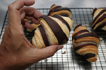 Fresh baked croissants with chocolate stripes cooling on a metal rack. Close-up view of golden brown pastry with flaky texture, homemade bakery concept.