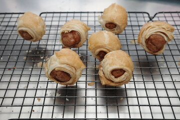freshly baked sausage roll pastry with flaky golden layers, placed over a cooling rack. Close-up view of homemade bakery snack, warm and appetizing food concept.