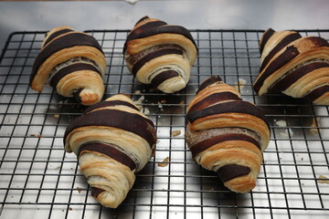 Fresh baked croissants with chocolate stripes cooling on a metal rack. Close-up view of golden brown pastry with flaky texture, homemade bakery concept.