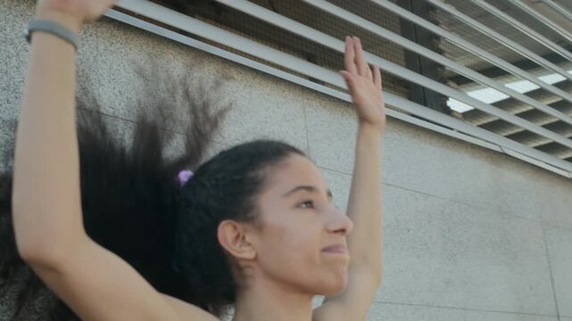 Young fit woman in active wear doing jumping jacks while exercising outdoors in city on summer day