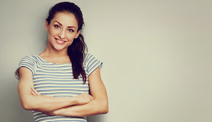 Fototapeta premium Cute toothy smiling young woman posing with folded arms in light blue sporty cotton t-shirt n blue studio background. Closeup toned front banner portrait