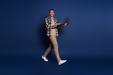 Full length photo of funky cool guy dressed plaid shirt walking texting modern device emtpy space isolated blue color background