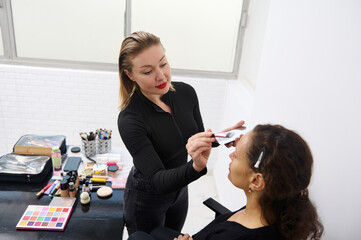 Professional makeup artist applying eyeshadow to a client in a bright studio