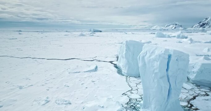 Calving icebergs towering winter arctic landscape. Snow covered Antarctic ocean surface. Blue ice floes stuck in frozen water, mountains in background. Polar cold scene. Antarctica travel exploration