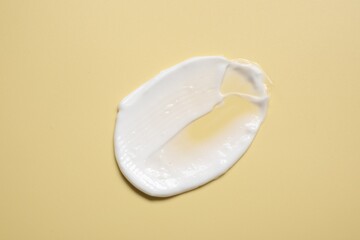 Face cream on pale yellow background, top view