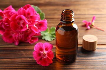 Geranium essential oil in bottle and beautiful flowers on wooden table