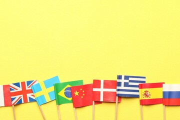 Obraz premium Small paper flags of different countries on yellow background, flat lay. Space for text