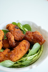Fried chicken breast in bite-sized pieces with greens in a white bowl close-up