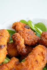 Fried chicken breast in bite-sized pieces with greens in a white bowl close-up