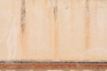 A weathered wall with streaks of water damage and a row of red bricks at the bottom