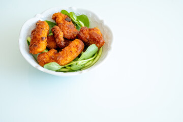 Fried chicken breast in bite-sized pieces with greens in a white bowl close-up